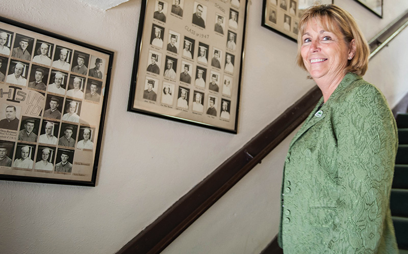 Barbara Fitzgerald, director of development for the Leavenworth Regional Catholic School System, stands in front of images of graduating classes dating back to the early 1900s that line the walls of Immaculata High School. Fitzgerald led the campaign this spring to raise $1 million and save Immaculata High School. Photo by Joe McSorley.