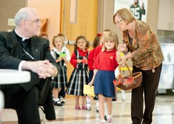 Samantha Gast, a kindergartner at Sacred Heart School in Ottawa, seems a little apprehensive about approaching Archbishop Joseph F. Naumann.  Kindergarten teacher Lisa McSwain tries to encourage Gast.