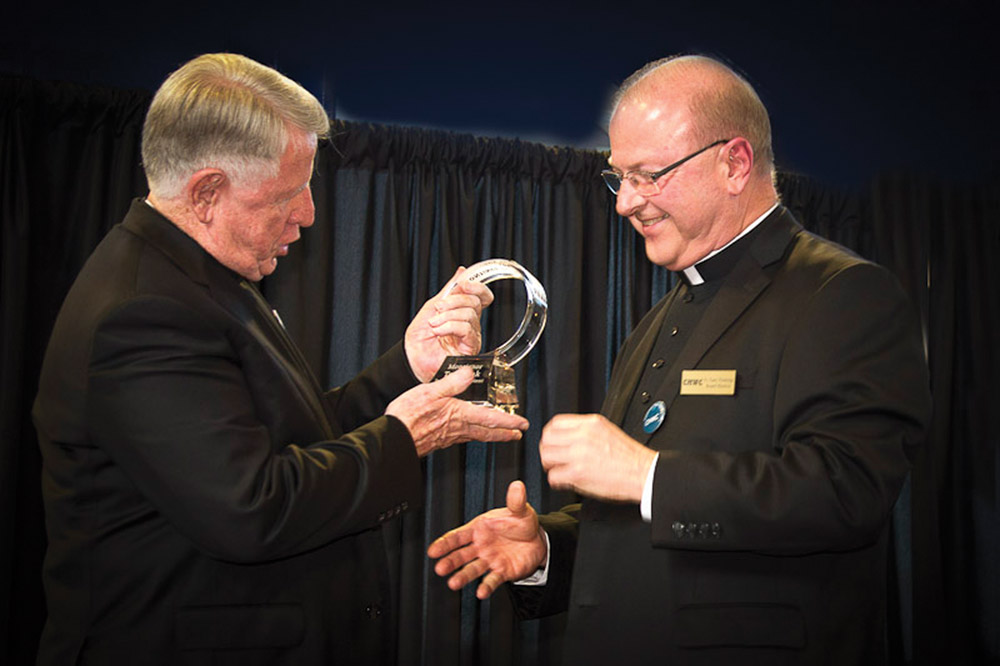 Photo by John Caulfield Father Gary Pennings (right), archdiocesan vicar general, hands Msgr. Thomas Tank with the first-ever Msgr. Thomas Tank Award from Community Housing of Wyandotte County. The award, which is expected to be presented annually, was presented at the Center Circle fundrasing event June 15 at Livestrong Sporting Park in Kansas City, Kan.