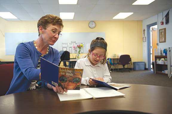 EAVEN PHOTO BY JESSICA LANGDON Jeanine Schneider, left, works with Bella DeBrevi, a sixth-grader at Holy Cross School in Overland Park. The DeBrevi family nominated Schneider for a Commitment to Excellence award this spring through the Down Syndrome Guild of Greater Kansas City. Schneider not only helps her students with reading skills, but fosters their independence and love of learning.