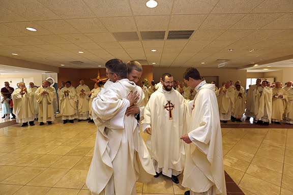 Following their ordination ceremony, Father Daniel Schmitz, Father Lawrence Bowers, Father Nathan Haverland and Father Quentin Schmitz exchange hugs as the priests of the archdiocese applaud in the background.
