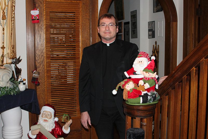 Father Tim Haberkorn stands ready to greet all comers in the main hallway of the rectory at Sacred Heart-St. Joseph Parish in Topeka, where he will hold his annual open house Dec. 14. Although the rectory will be decked out for the season in his personal collection of Christmas memorabilia, he has an extensive relic collection as well.