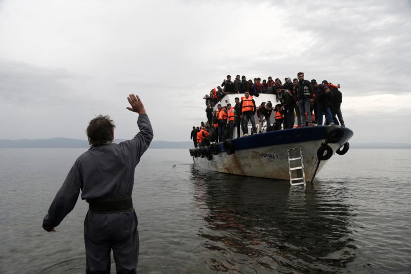 A resident waves to an overcrowded fishing boat carrying migrants after they arrived on the Greek island of Lesbos Oct. 11 after crossing the Aegean sea from Turkey. Greece is bracing for thousands more Syrian and other migrants to land on Lesbos and other key island crossings from Turkey, as those fleeing conflict remain undeterred by the worsening weather and colder autumn temperatures. (CNS photo/Yannis Kolesidis, EPA)