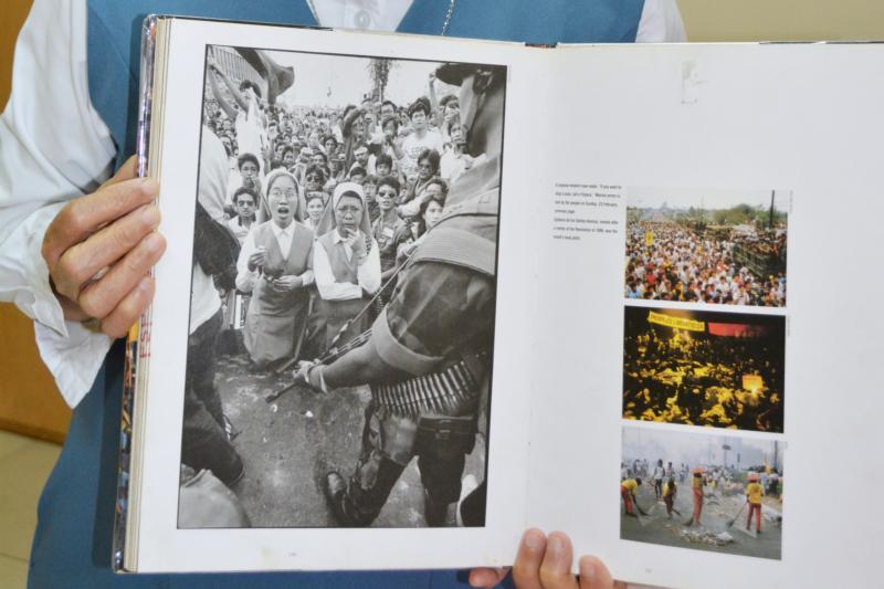 Sister Porferia Ocariza, a member of the Daughters of St. Paul, holds a book on the People Power uprising in the Philippines 30 years ago to oust dictator Ferdinand Marcos.  She is still recognized today for her stunned expression, left image, as military tanks approached. (CNS photo/Simone Orendain)