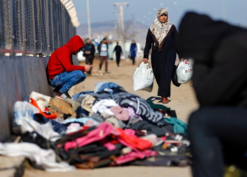 A refugee woman from Syria carries food while other displaced people sit near a border gate in Kilis, Turkey, Feb. 9. More than 30,000 people are stranded in northern Aleppo province after Turkish government forces closed border crossings. (CNS photo/Sedat Suna, EPA)