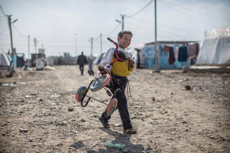 An Iraqi boy smiles as he carries a tricycle in a Baghdad camp for those internally displaced Feb. 3. (CNS photo/Oliver Weiken, EPA)