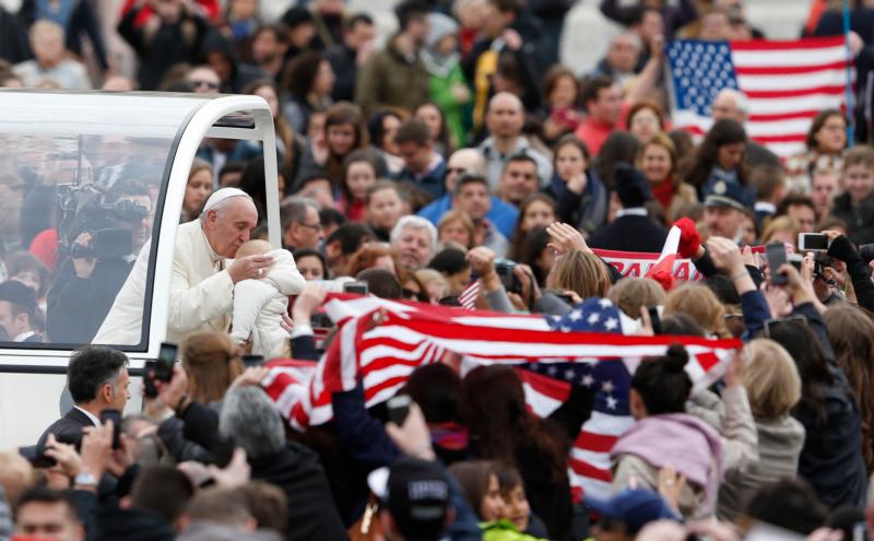U.S. flags are seen as Pope Francis kisses a baby during his general audience in St. Peter's Square at the Vatican March 23. (CNS photo/Paul Haring)